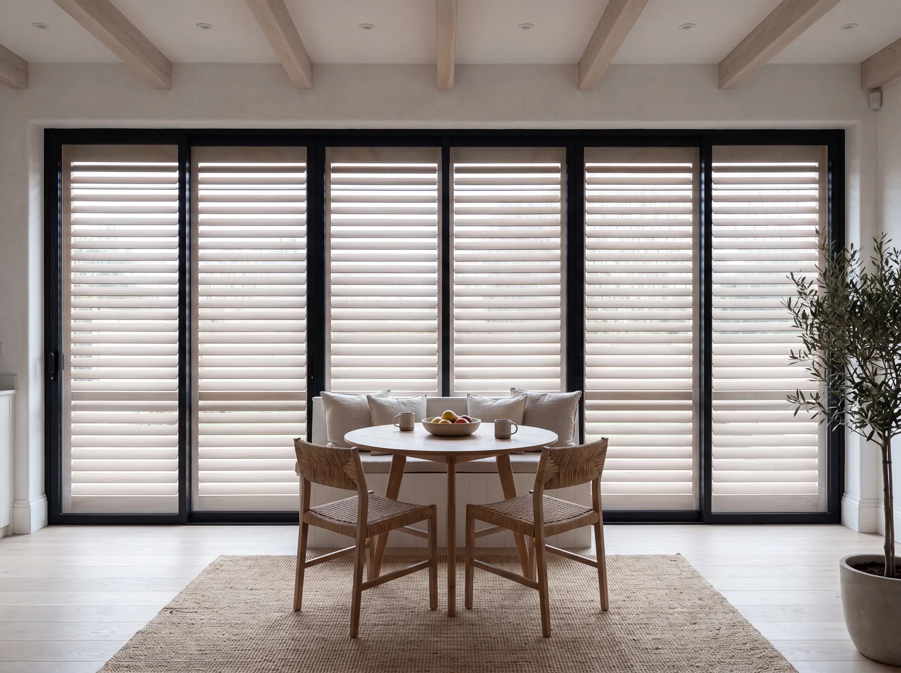Plantation shutters across a wall of black-framed sliding doors, behind a round breakfast table